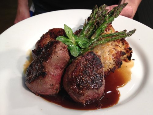 A plate of seared beef tenderloin with asparagus and a crispy bread slice, garnished with fresh basil.