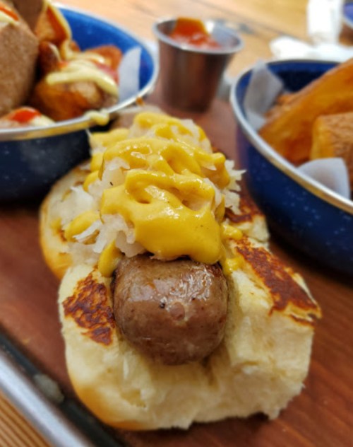 A close-up of a grilled sausage in a toasted bun, topped with mustard and sauerkraut, served with fries and ketchup.