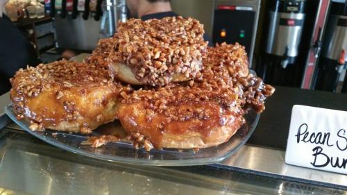 A plate of pecan sticky buns topped with caramel and chopped pecans, displayed in a bakery.