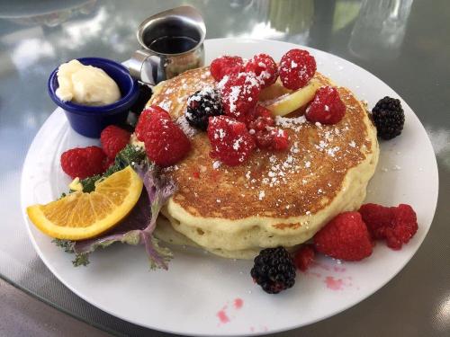 A fluffy pancake topped with fresh raspberries, blackberries, lemon, powdered sugar, and served with syrup and cream.
