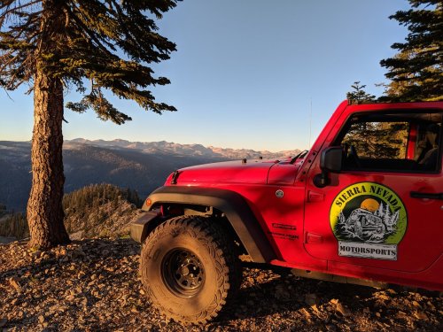 A red Jeep parked near a tree, overlooking a mountain range at sunset in the Sierra Nevada.