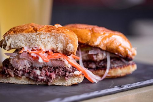 Two delicious sandwiches on a slate plate, featuring layers of meat, fresh vegetables, and soft, golden-brown buns.