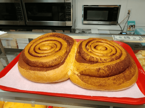 A large, freshly baked cinnamon roll on a red tray, featuring two spiral-shaped sections with a golden-brown crust.