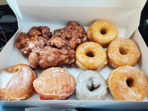 A box of assorted donuts, including glazed, apple fritters, and sugar-coated varieties.