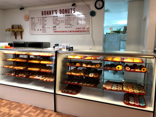 Display case filled with various donuts at Bonny's Donuts, featuring colorful toppings and a menu in the background.