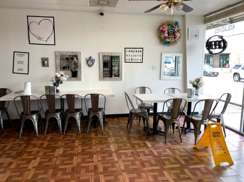 A cozy café interior with metal chairs, tables, mirrors, and decorative wall art. A caution sign is visible on the floor.