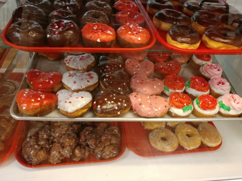 A display of assorted donuts, including chocolate-covered, heart-shaped, and decorated varieties on red trays.