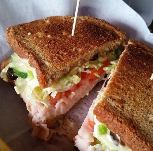 A close-up of a sandwich with turkey, lettuce, tomato, and green peppers on whole grain bread, secured with a toothpick.