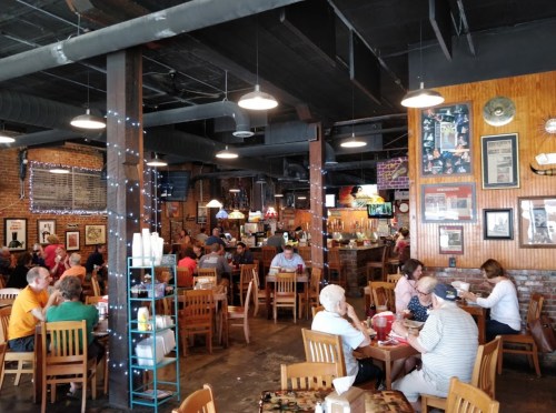 A bustling restaurant interior with diners at tables, brick walls, and decorative lights.