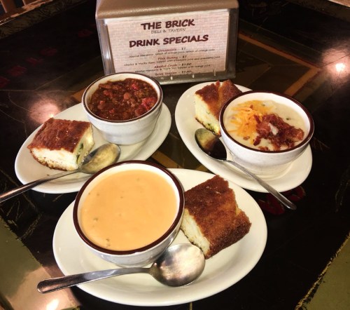Four bowls of soup and chili with cornbread, placed on a table next to a menu of drink specials.
