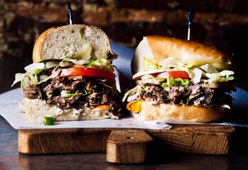 A close-up of a hearty sandwich filled with beef, lettuce, tomatoes, and peppers, served on a toasted bun.
