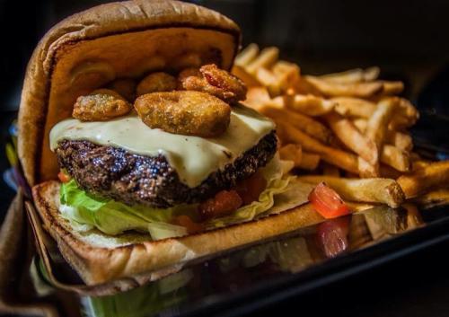 A close-up of a burger with cheese, lettuce, and fried pickles, served with a side of golden French fries.