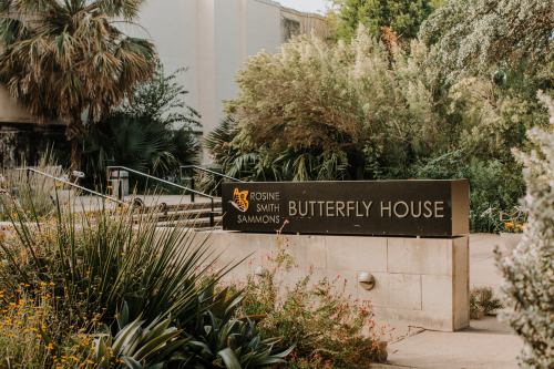 Sign for the Rosine Smith Sammons Butterfly House, surrounded by lush greenery and colorful flowers.