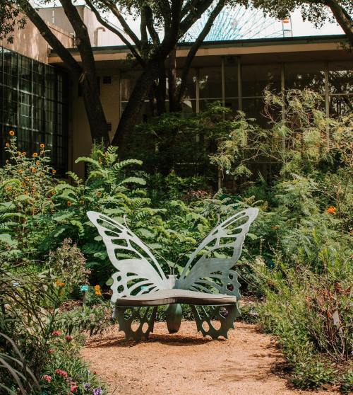 A butterfly-shaped bench surrounded by lush greenery and colorful flowers in a serene garden setting.