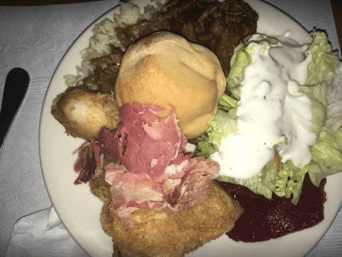 A plate of food featuring fried chicken, sliced meat, a roll, rice, salad with dressing, and a side of jelly.