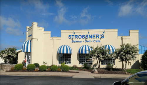 Exterior of Strossner's Bakery, Deli, and Cafe featuring blue and white striped awnings and landscaped surroundings.