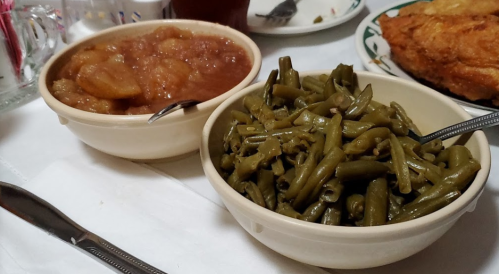 Two bowls of food: one with green beans and the other with apple sauce, served on a white tablecloth.