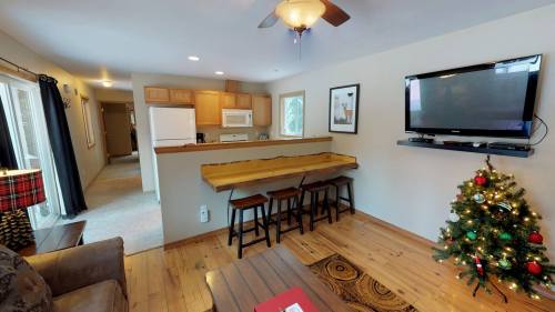 Cozy living area with a kitchen bar, stools, and a decorated Christmas tree in a well-lit room.
