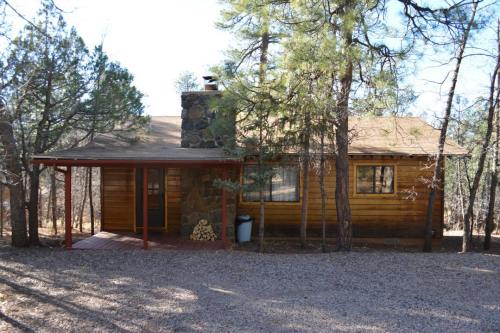 A cozy wooden cabin with a stone chimney, surrounded by trees and gravel, set in a serene outdoor environment.