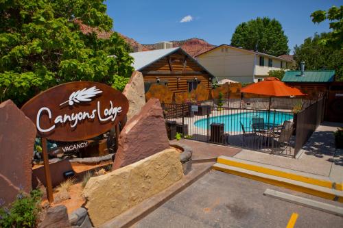 Canyons Lodge sign in front of a pool area with lounge chairs and orange umbrellas, surrounded by greenery and buildings.