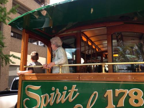 A child and an elderly woman stand on a vintage trolley, enjoying the view from the open back.
