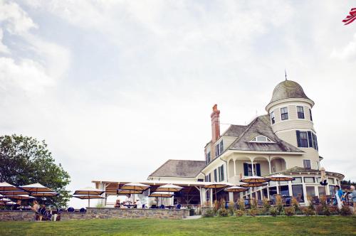 A large, elegant building with a turret, surrounded by umbrellas and greenery, under a cloudy sky.