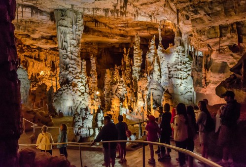 Visitors explore a stunning cave filled with stalagmites and stalactites, illuminated by warm lighting.