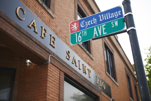 Street sign for 16th Ave SW at Czech Village, with the Cafe Saint Pio building in the background.