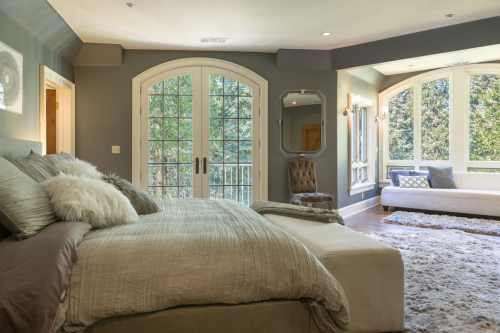 Cozy bedroom with a large bed, plush decor, and windows overlooking a green landscape. Soft lighting enhances the ambiance.