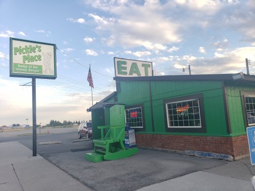 A green restaurant building with a sign reading "Pickle's Place" and "Home of the Atomic Burger," under a cloudy sky.