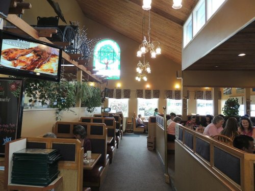 Interior of a cozy restaurant with wooden decor, booths, and a large window featuring a stained glass design.