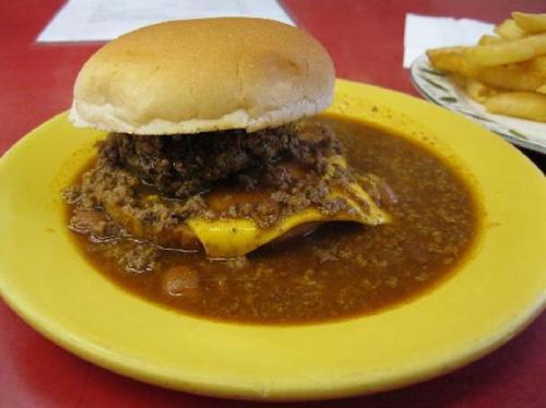 A cheeseburger topped with chili on a yellow plate, accompanied by a side of fries.