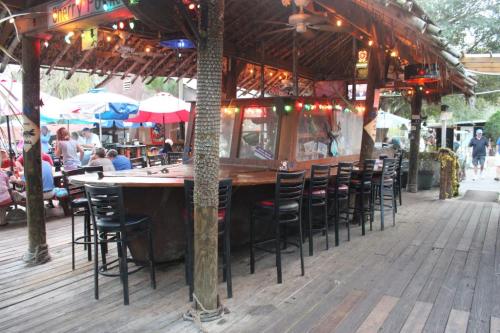 A rustic outdoor bar with wooden seating, colorful umbrellas, and patrons enjoying the lively atmosphere.