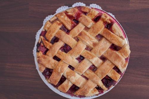A freshly baked cherry pie with a lattice crust, resting on a lace doily on a wooden surface.