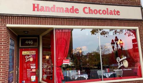 A storefront with a sign reading "Handmade Chocolate," featuring red curtains and a "Closed" sign in the window.