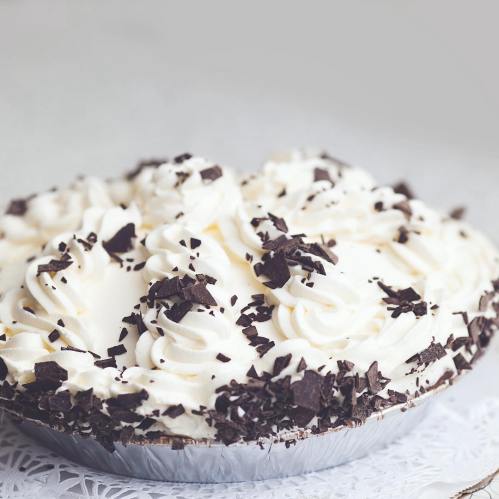 A creamy pie topped with whipped cream and chocolate shavings, presented on a lace doily.