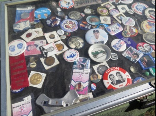 A display case filled with various political buttons, pins, and memorabilia, including Nixon and Boston Red Sox items.
