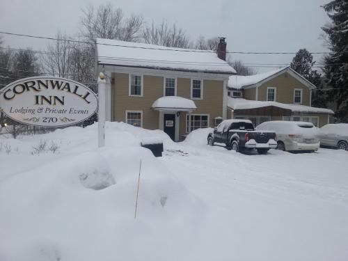 A snow-covered Cornwall Inn with a sign, surrounded by deep snow and parked cars in winter.