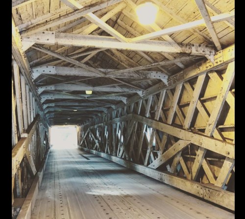 A view inside a wooden covered bridge, showcasing its intricate beams and a bright light at the far end.