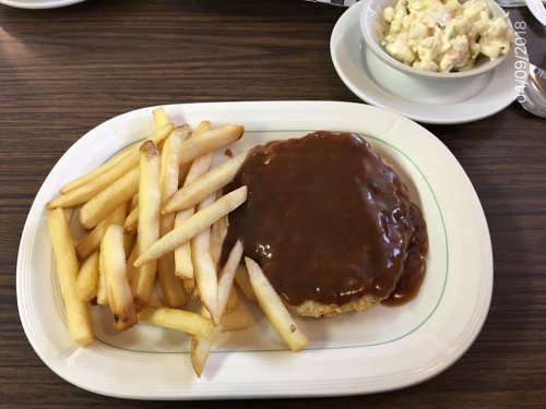 A plate with fries, a breaded patty covered in brown gravy, and a side of macaroni salad.