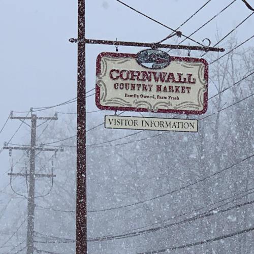 Sign for Cornwall Country Market, featuring "Visitor Information," amidst falling snow and a wintery scene.