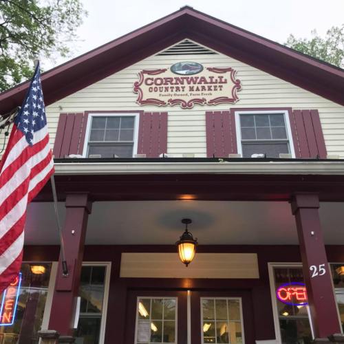 Front view of Cornwall Country Market, featuring a sign, American flag, and welcoming entrance with open sign.