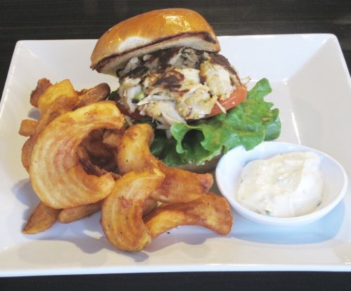 A delicious burger with lettuce and tomato, served with curly fries and a side of dipping sauce on a white plate.