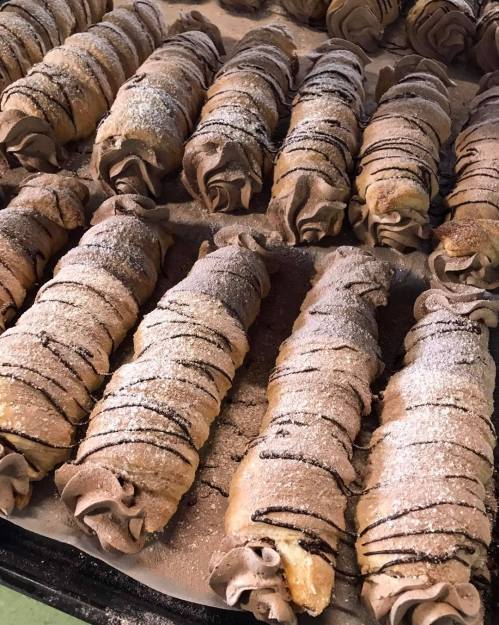 A tray of chocolate-filled pastries, dusted with powdered sugar and drizzled with chocolate, arranged neatly.