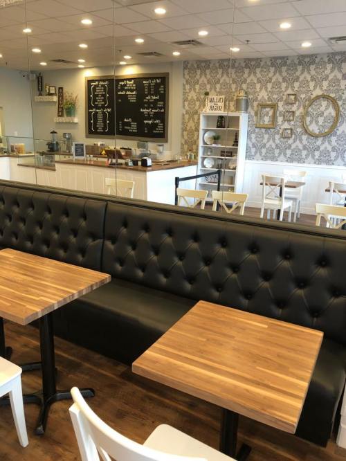 Cozy café interior with black tufted seating, wooden tables, and a decorative wall featuring a menu board.