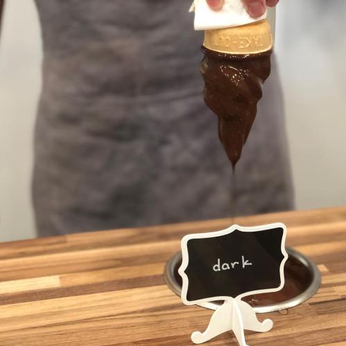 A hand holding a cone with dark chocolate ice cream, dripping slightly, next to a sign labeled "dark."