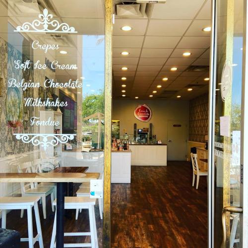A cozy dessert shop entrance featuring a menu of crepes, ice cream, milkshakes, and fondue. Bright and inviting interior.