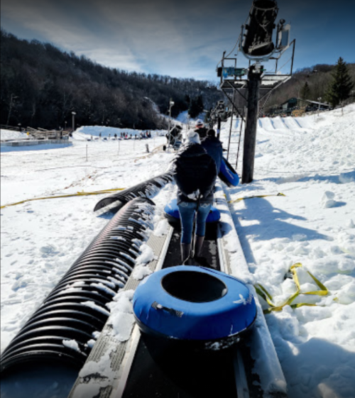 A snowy landscape with people walking towards a ski lift, carrying blue inner tubes for tubing.