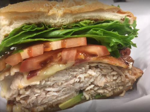 A close-up of a sandwich with layers of turkey, lettuce, tomato, and bacon on a toasted bun.