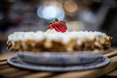 A close-up of a dessert pie topped with whipped cream and a strawberry, set on a decorative plate.